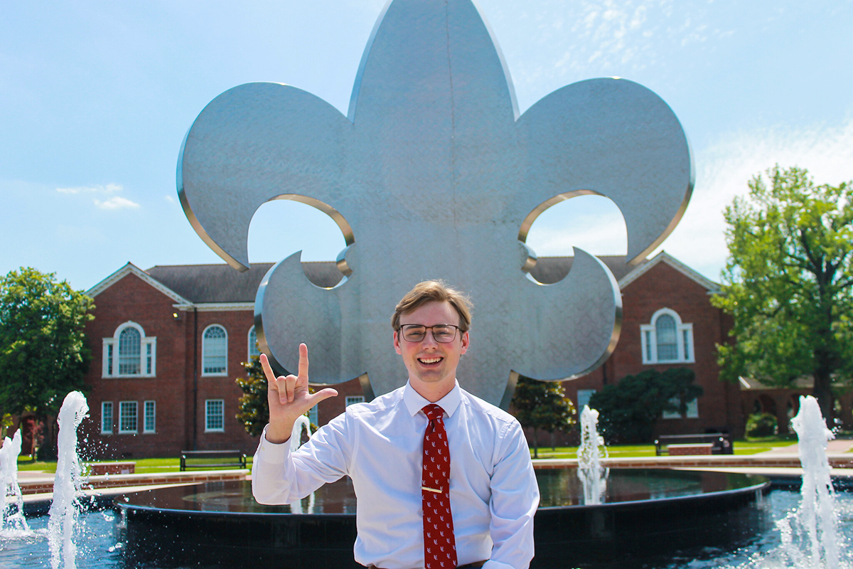 Education major Dylan Hebert holding up the UL hand sign in front of the University of Louisiana Quad fountain